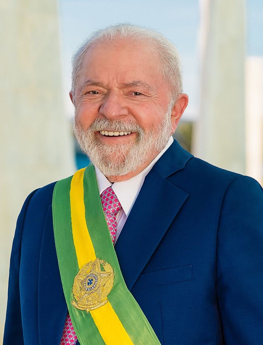Smiling older man in suit wearing green-and-yellow presidential sash, close-up portrait